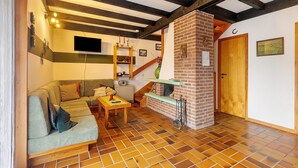 A cozy living room with a sofa, a wooden table, a brick fireplace, and a staircase.