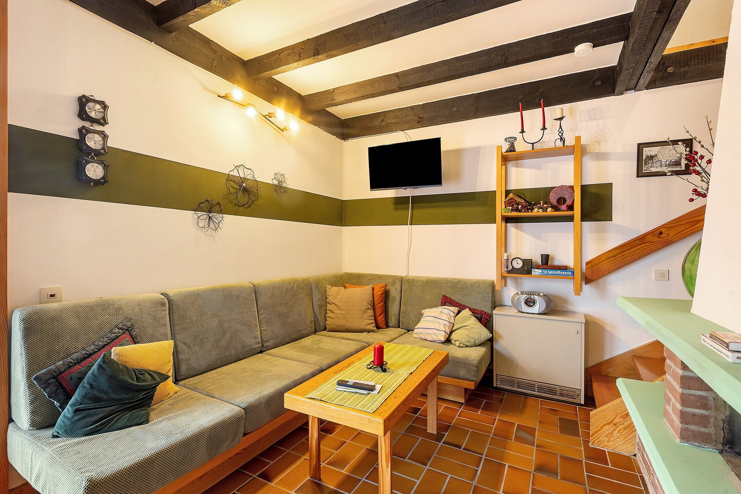 A living room with a sofa, a small table, a television, and a wooden shelf with decorative items.