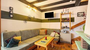 A living room with a sofa, a small table, a television, and a wooden shelf with decorative items.