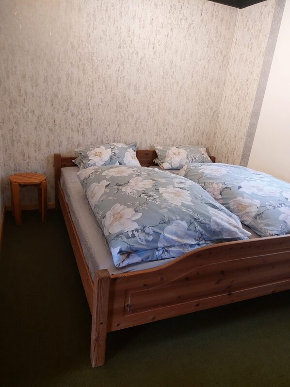 Una cama de madera con ropa de cama floral en una habitación con papel tapiz texturizado.