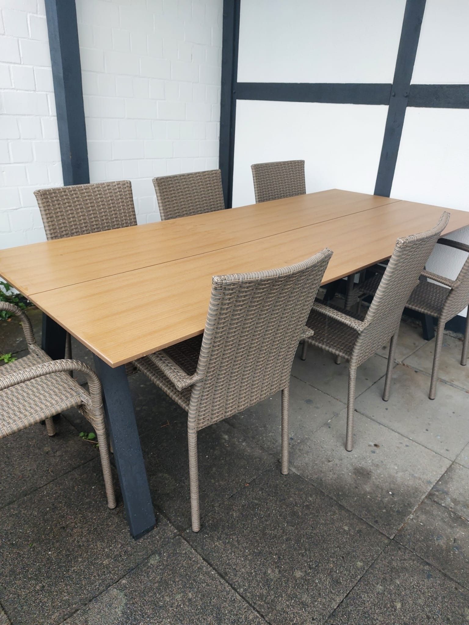 Una mesa rectangular al aire libre con seis sillas de mimbre.