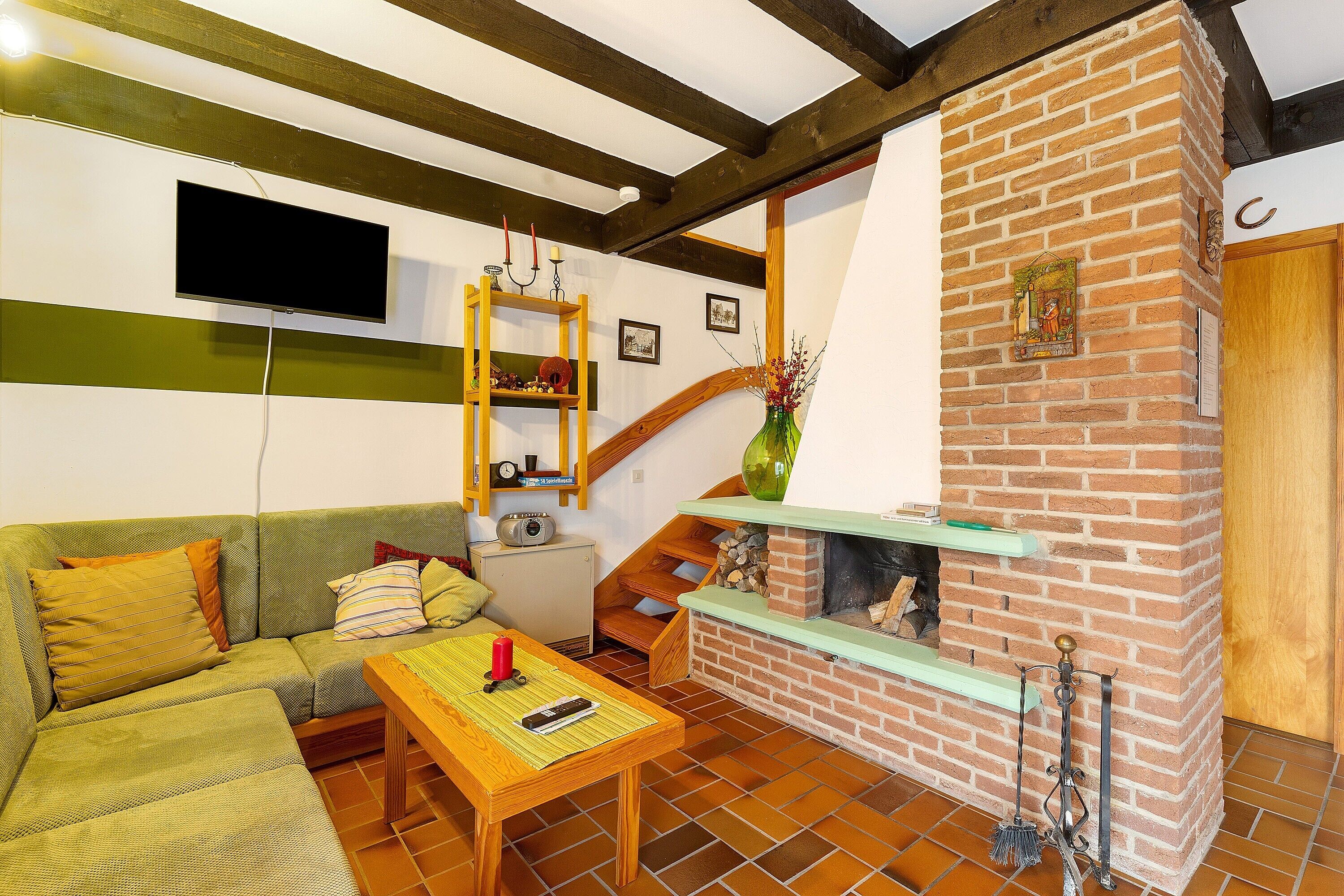 A living room with a green sofa, a wooden table, a brick fireplace, and a staircase.