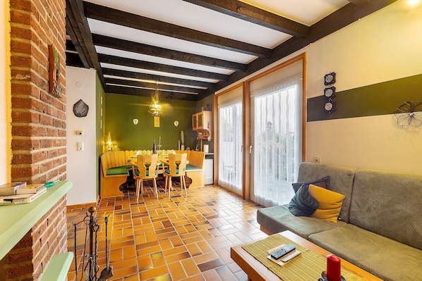 Un espace repas avec un mur en briques, des poutres en bois au plafond et un mur vert orné d’une horloge.