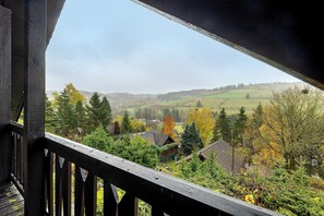 Un balcón de madera con vistas a un paisaje rural con casas, árboles y colinas ondulantes.