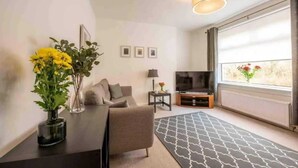 Ett modernt vardagsrum med en soffa, en tv, en lampa och ett fönster med utsikt.