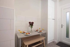Una piccola cucina con piastrelle bianche, una panca in legno e un tavolo apparecchiato con piatti e bicchieri.