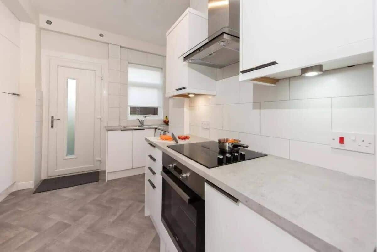 A modern kitchen with white cabinetry, a black induction cooktop, and a built-in oven.