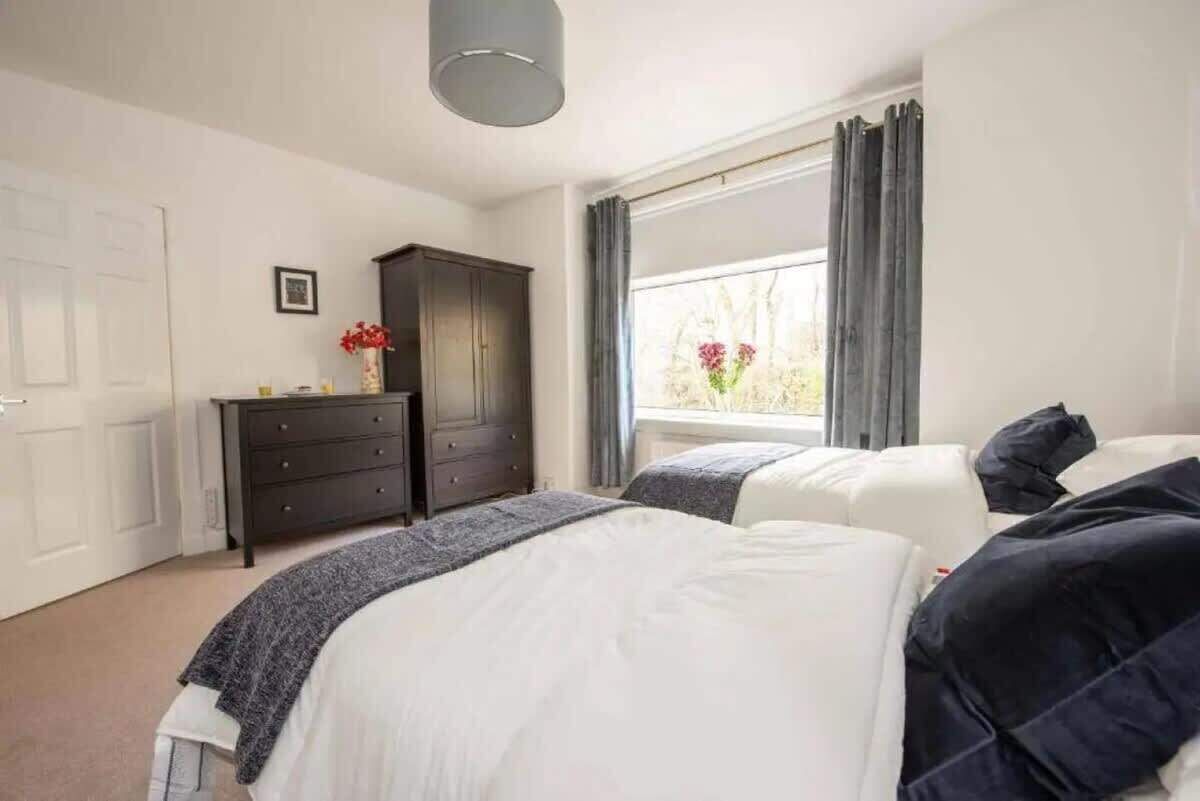 A bedroom with two beds, a dresser, a window with curtains, and a door.