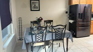A dining area with a table set for four, a chandelier, a framed picture on the wall, and a refrigerator in the background.