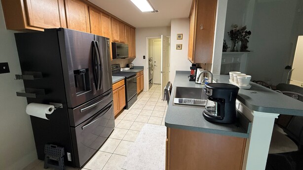A modern kitchen with wooden cabinets, a stainless steel refrigerator, a microwave, and a coffee maker.