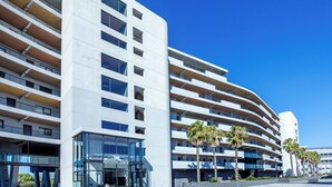 Een modern hotel met een gebogen gevel, meerdere balkons en een opvallende entree met glazen deuren.