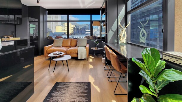Ein modernes Wohnzimmer mit einer Couch, einem Couchtisch und Blick auf die Stadt durch große Fenster.