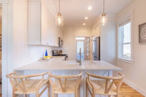 A kitchen with white cabinets, a large island with bar stools, stainless steel appliances, and pendant lighting.