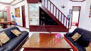 A living room with two black leather sofas, a wooden coffee table, and a staircase with a wooden railing. - Hotel O Bougenville Resort (Cipanas)
