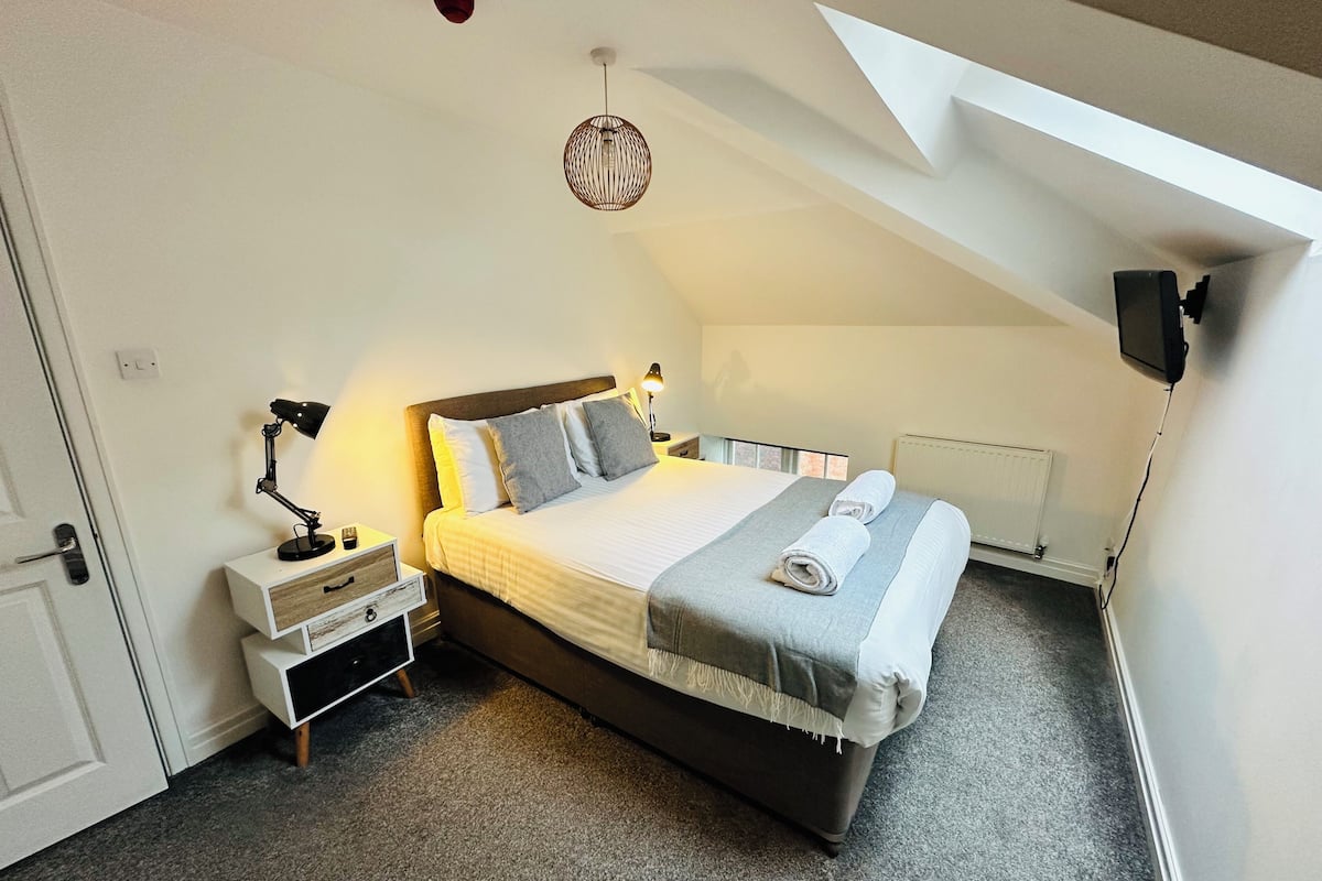Une chambre avec un grand lit, des tables de chevet, un luminaire suspendu et une vue sur le ciel grâce à une lucarne.