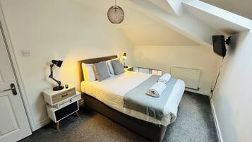 A bedroom with a large bed, bedside tables, a hanging light fixture, and a view through a skylight.
