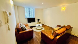 A modern living room with two leather sofas, a coffee table, a flat-screen TV, and a small side table. - West Street Mews Serviced Accommodation (Exeter)