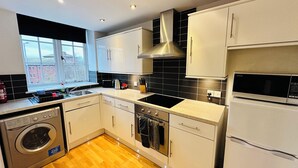 A modern kitchen with a washing machine, dishwasher, microwave, and a large window offering a view of the city. - West Street Mews Serviced Accommodation (Exeter)