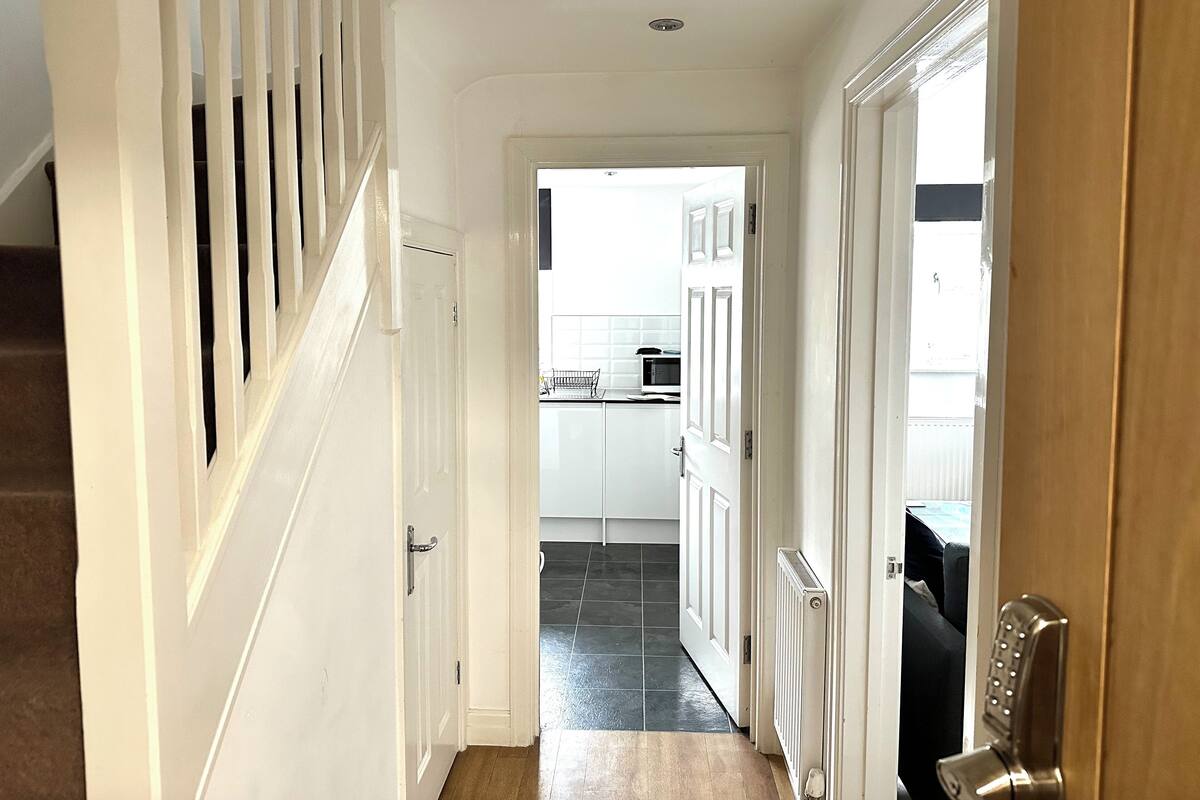 Un couloir avec un escalier en bois sur la gauche, une porte blanche sur la droite et, au fond, un espace cuisine.