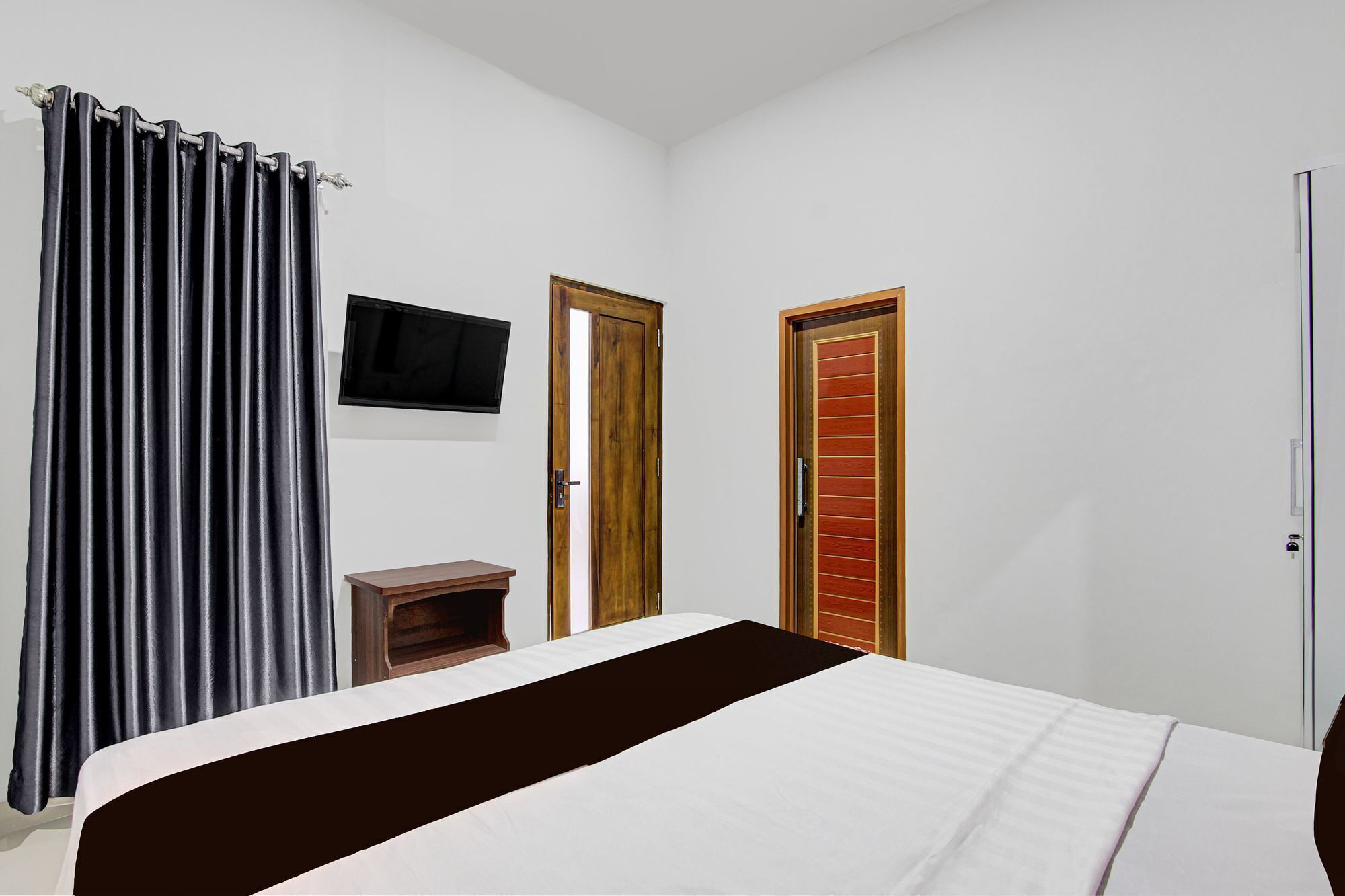 Un dormitorio con una cama, un televisor montado en la pared y dos puertas.