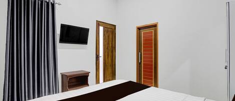 Un dormitorio con una cama, un televisor montado en la pared y dos puertas.