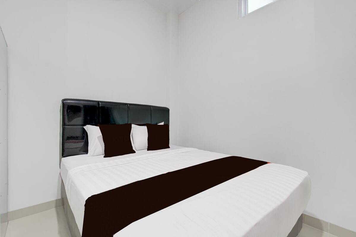 Un dormitorio moderno con una cama grande, paredes blancas y un cabecero oscuro.