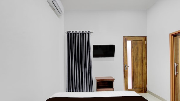 A bedroom with a bed, a small wooden nightstand, a black and white striped curtain, a mounted TV, and a wooden door.