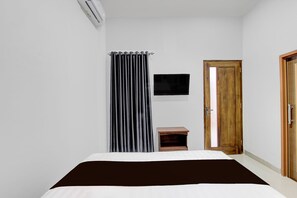 Une chambre à coucher avec un lit, une petite table de chevet en bois, un rideau rayé noir et blanc, un téléviseur fixé au mur et une porte en bois.