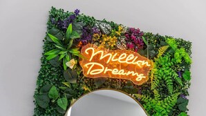 Une enseigne au néon portant l’inscription « Million Dreams » et entourée d’un feuillage verdoyant et luxuriant.