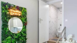 Un escalier avec des marches en bois et une rampe, menant à une pièce dont un mur est recouvert de marbre blanc et qui possède une porte blanche.