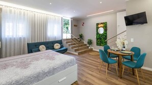Une chambre d’hôtel moderne comprenant un lit, un canapé, un coin repas avec des chaises, un escalier et un téléviseur fixé au mur.