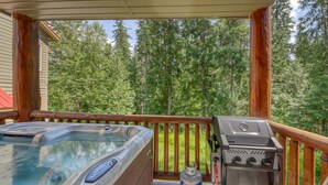 A hot tub and grill on a wooden deck with a view of a forest. - Ski-in Townhome - Private Hot Tub - Fernie Resort (Fernie)