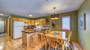 A kitchen with wooden cabinets, a central island, bar stools, and a dining table with chairs. - Ski-in Townhome - Private Hot Tub - Fernie Resort (Fernie)