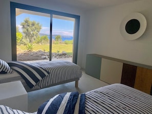 A bedroom with two beds, a large window with a view of a garden and a body of water, and a round wall decoration. - NEAR ST TROPEZ, MAGNIFICENT VILLA WITH SEA VIEW, SWIMMING POOL, CLOSE TO BEACHES. (Cavalaire-sur-Mer)