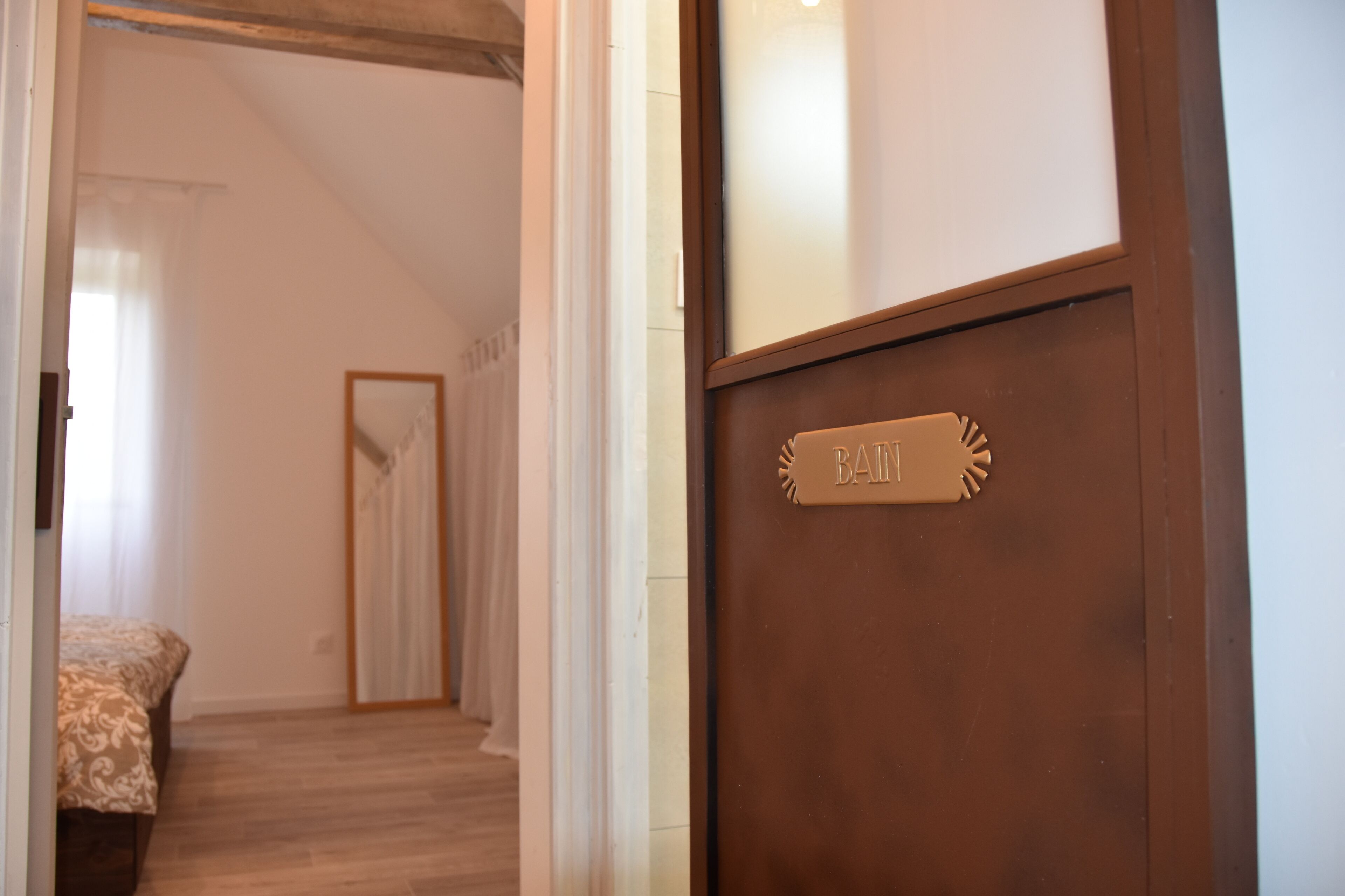 Habitación de hotel con una puerta de madera que indica “BAIN” y una cama con una colcha estampada.