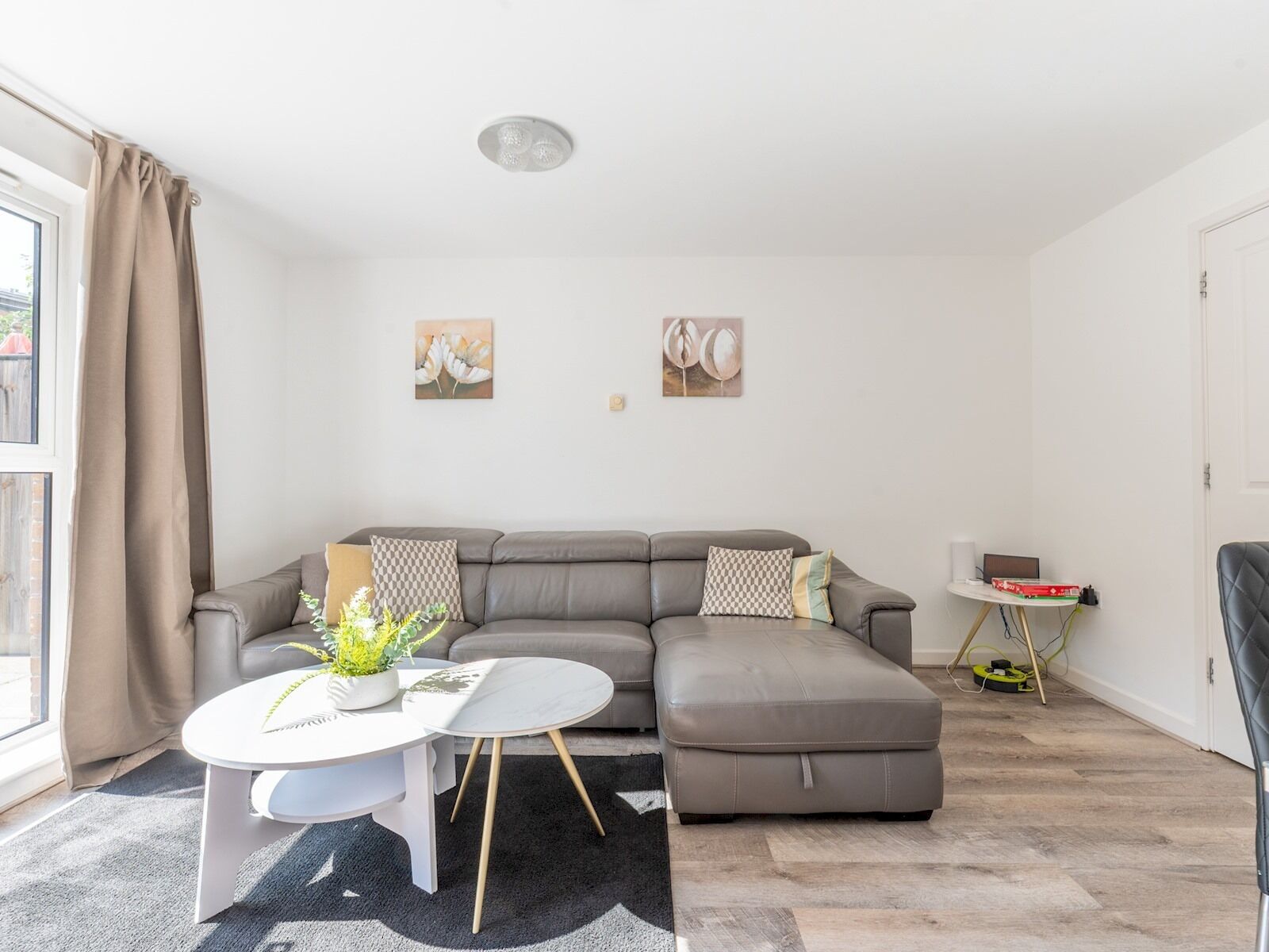 Un salon moderne avec un canapé d’angle gris, une table basse ronde blanche et une petite table d’appoint sur laquelle se trouvent un ordinateur portable et une boîte rouge.
