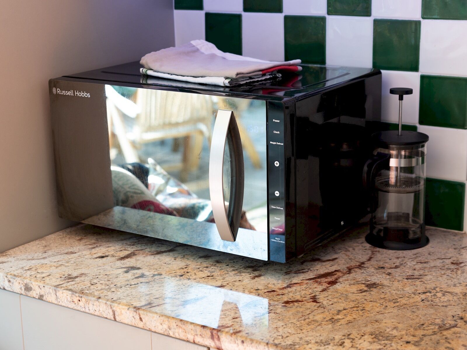 Een compact magnetron met een digitaal display, een waterdispenser van roestvrij staal en een geruit spatwand.