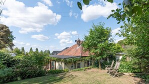 A house with a sloped roof, surrounded by a garden with various plants and a lawn. - Pass the Keys | Charming 3-Bed Bungalow with Character & Garden (London)