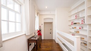 Un couloir doté d’un plancher en bois, de murs blancs et d’une étagère blanche contenant des livres et des récipients.