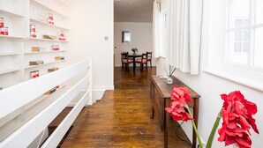 Un couloir avec des étagères blanches, un plancher en bois et un coin repas comprenant des chaises et une table.