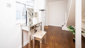 Une pièce lumineuse et bien éclairée, avec un plancher en bois, une table en verre et un banc rembourré, un radiateur blanc et une plante en pot.