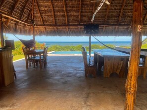 An outdoor seating area with a thatched roof, wooden furniture, and a view of the ocean. - Rancho Agua Fria, 3-bedroom House (Jucuaran)