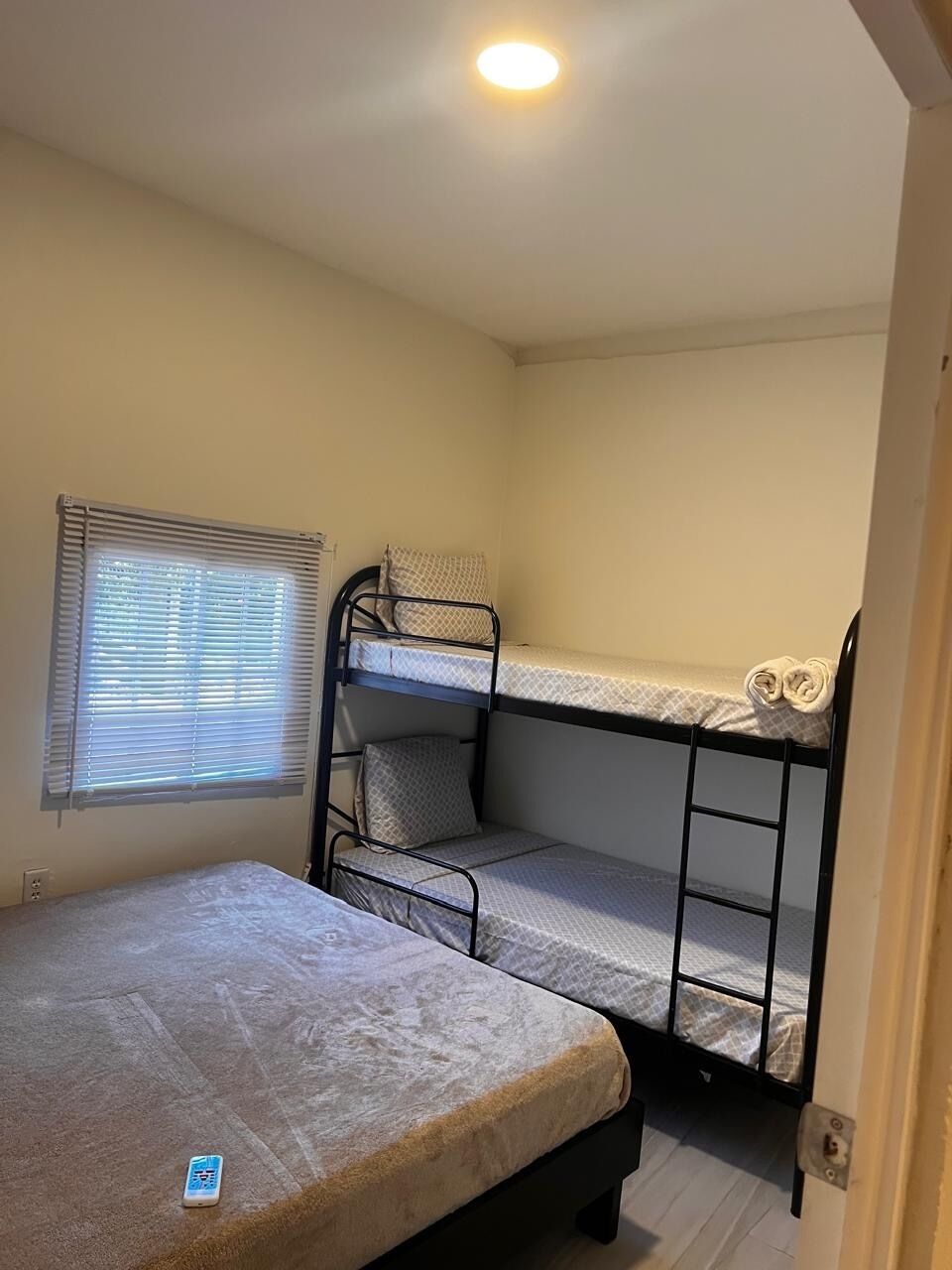 Une chambre avec des lits superposés, une fenêtre avec des stores et un matelas posé sur le sol.