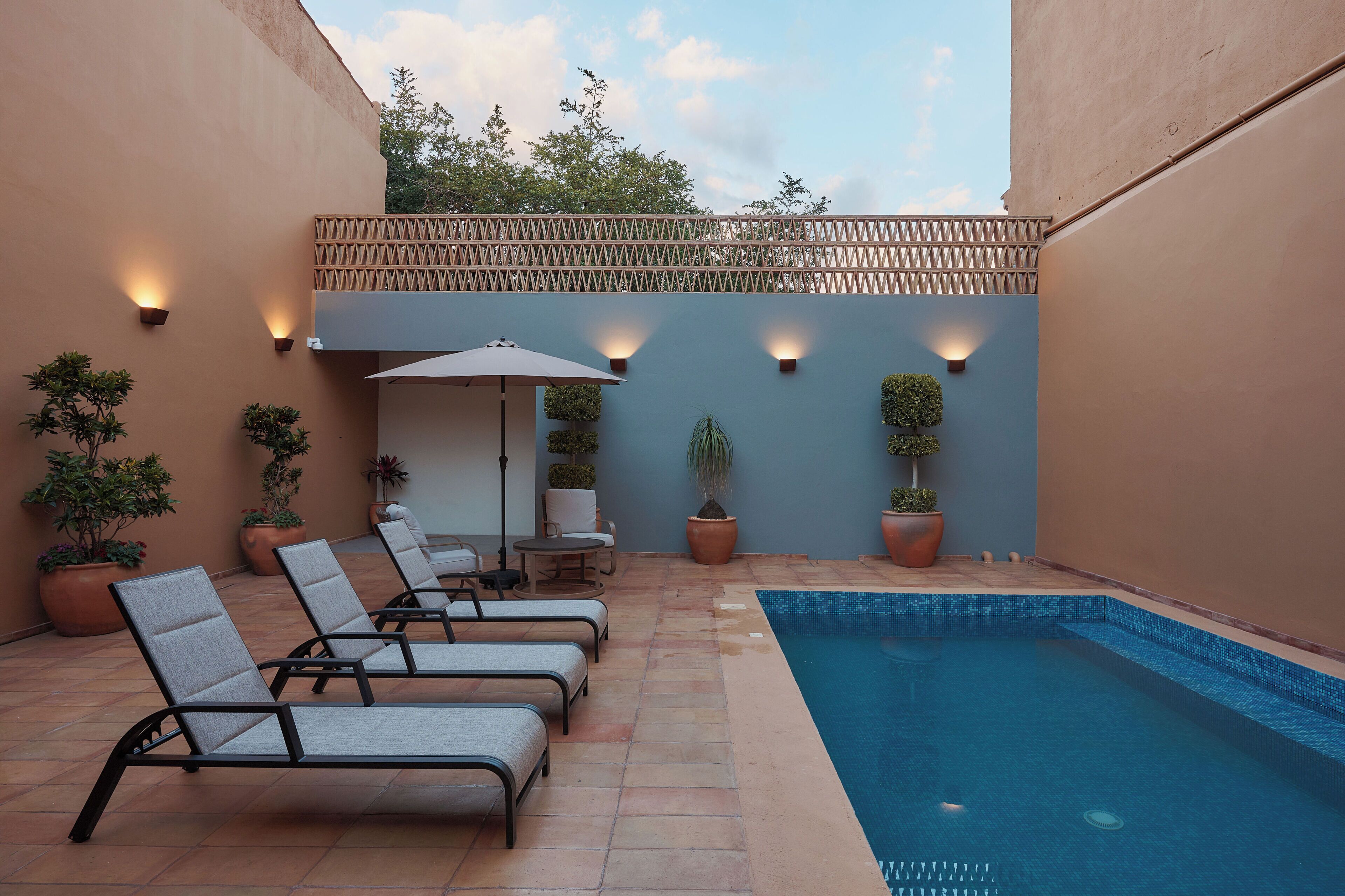 A poolside area with lounge chairs, a table, and potted plants.