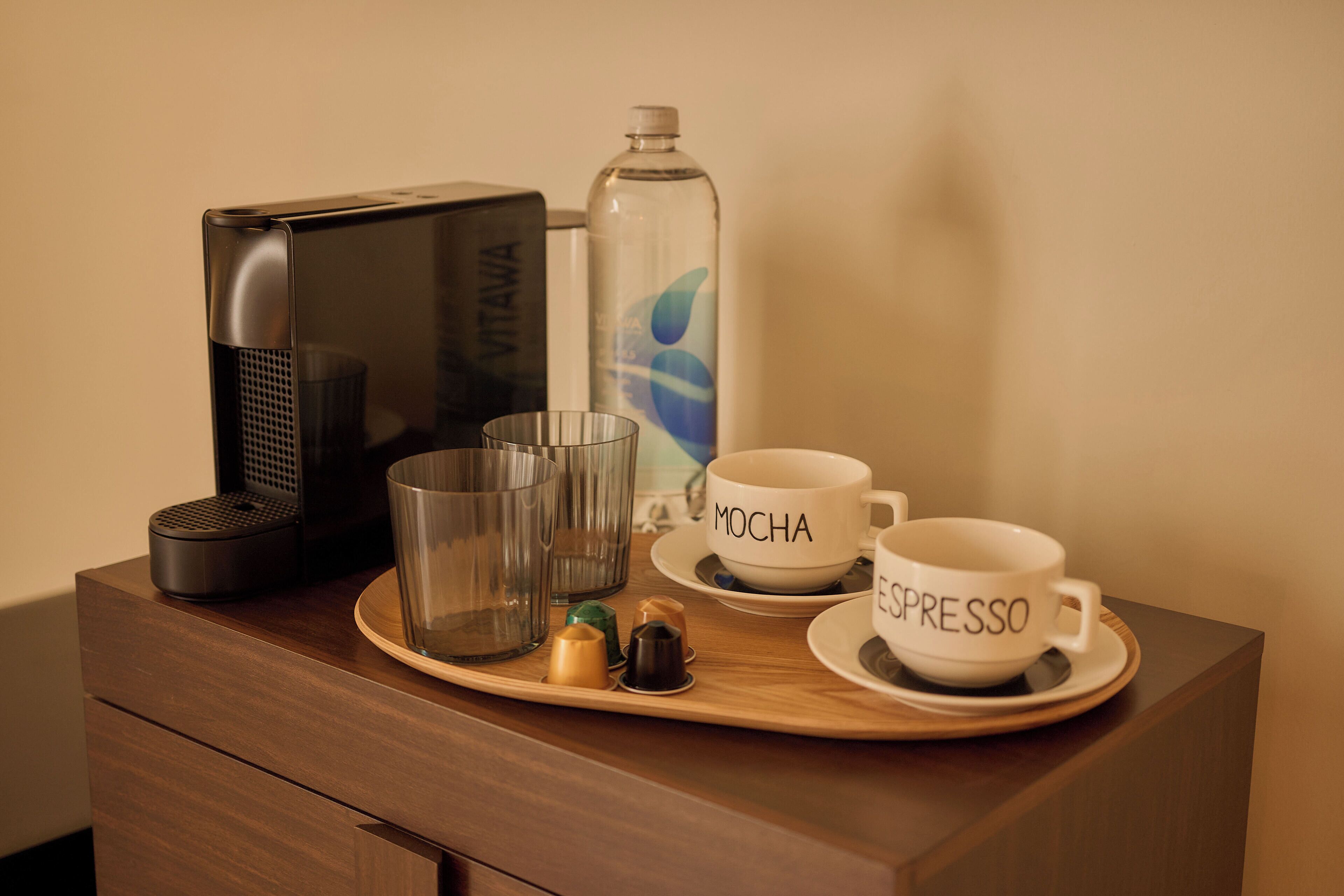 A coffee station with a coffee maker, a water bottle, and two cups labeled 'MOCHA' and 'ESPRESSO' on a wooden tray.