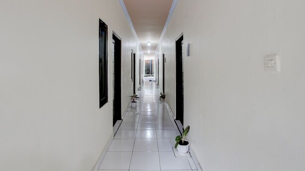 A long, narrow hallway with white walls and tiled floors, leading to a room with a window. - Hotel O Khayla Homestay Syariah (Giripurwo)