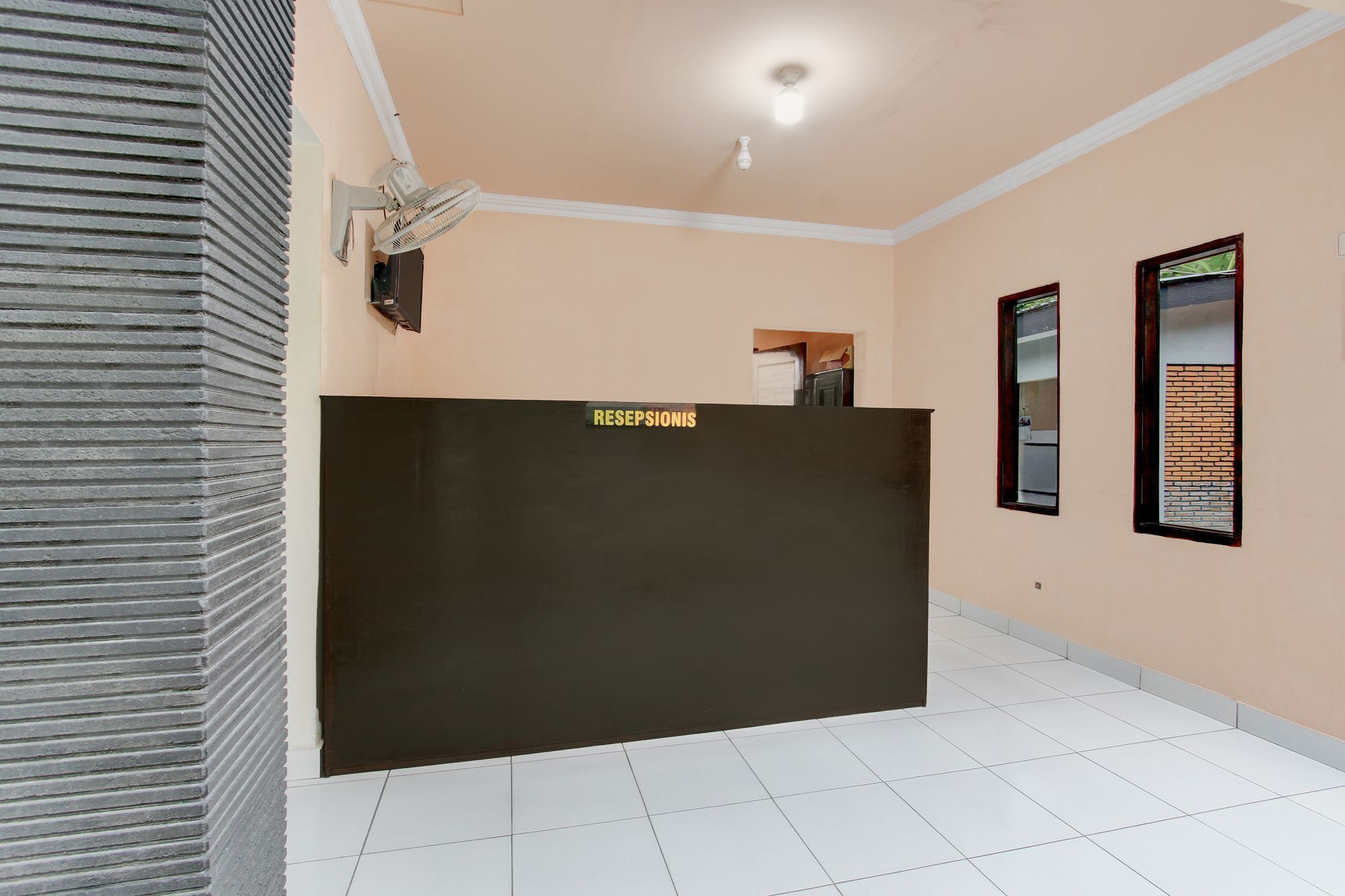 A reception area with a black reception desk, white tiled floor, and two windows with brick patterns.