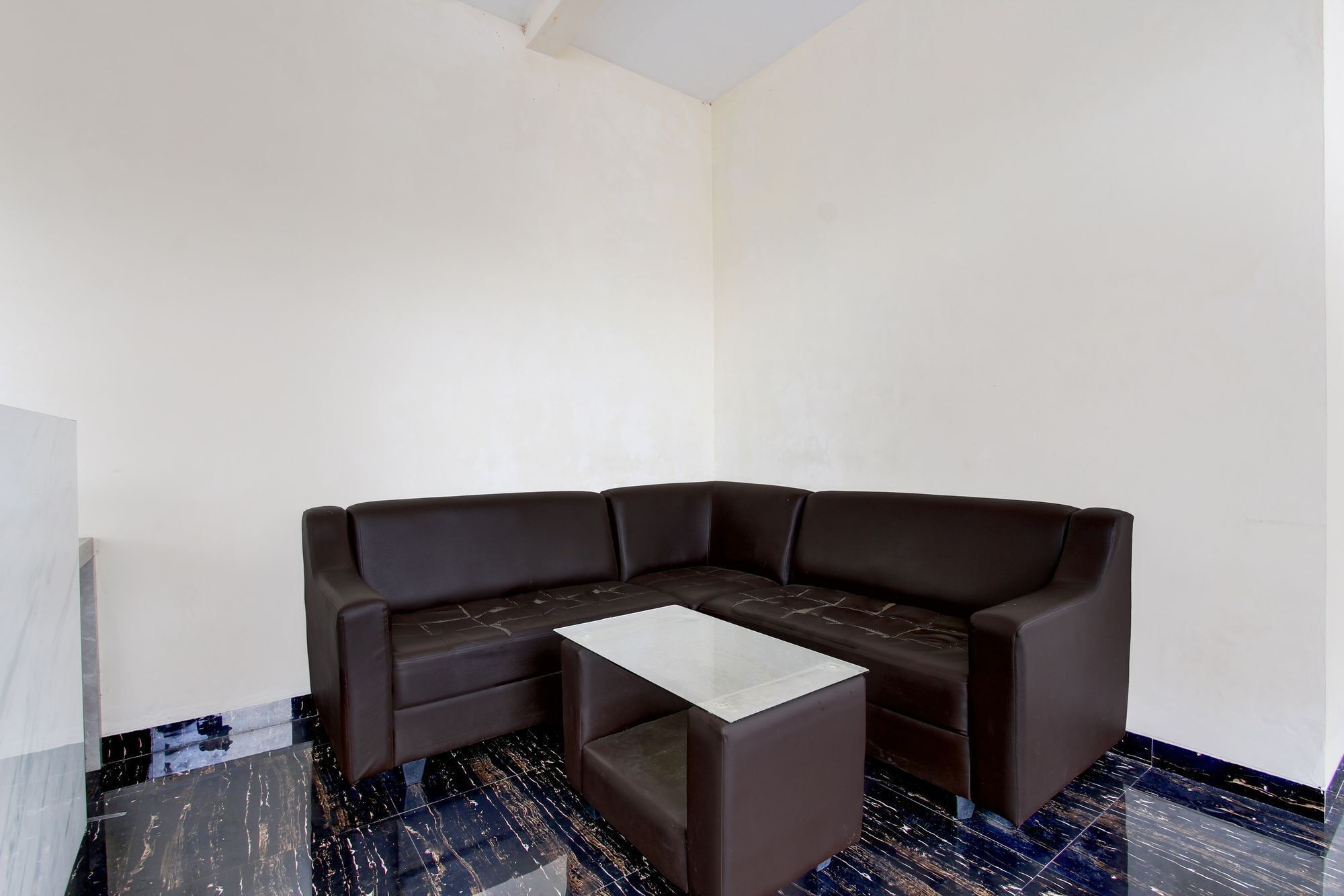 Una sala de estar con esquina, un sofá seccional de cuero marrón oscuro, una mesa de centro blanca y un piso de baldosas con diseño de mármol.