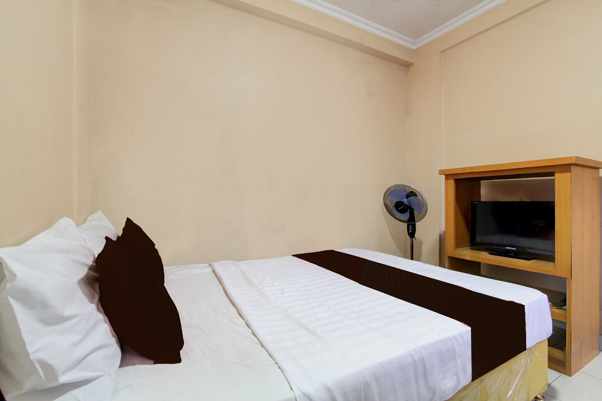Una camera d'albergo con un letto, una televisione su un mobile in legno e una ventola da terra.