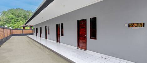 A long corridor with a series of doors, a sign for 'Parkir Motor', and a brick wall on one side.